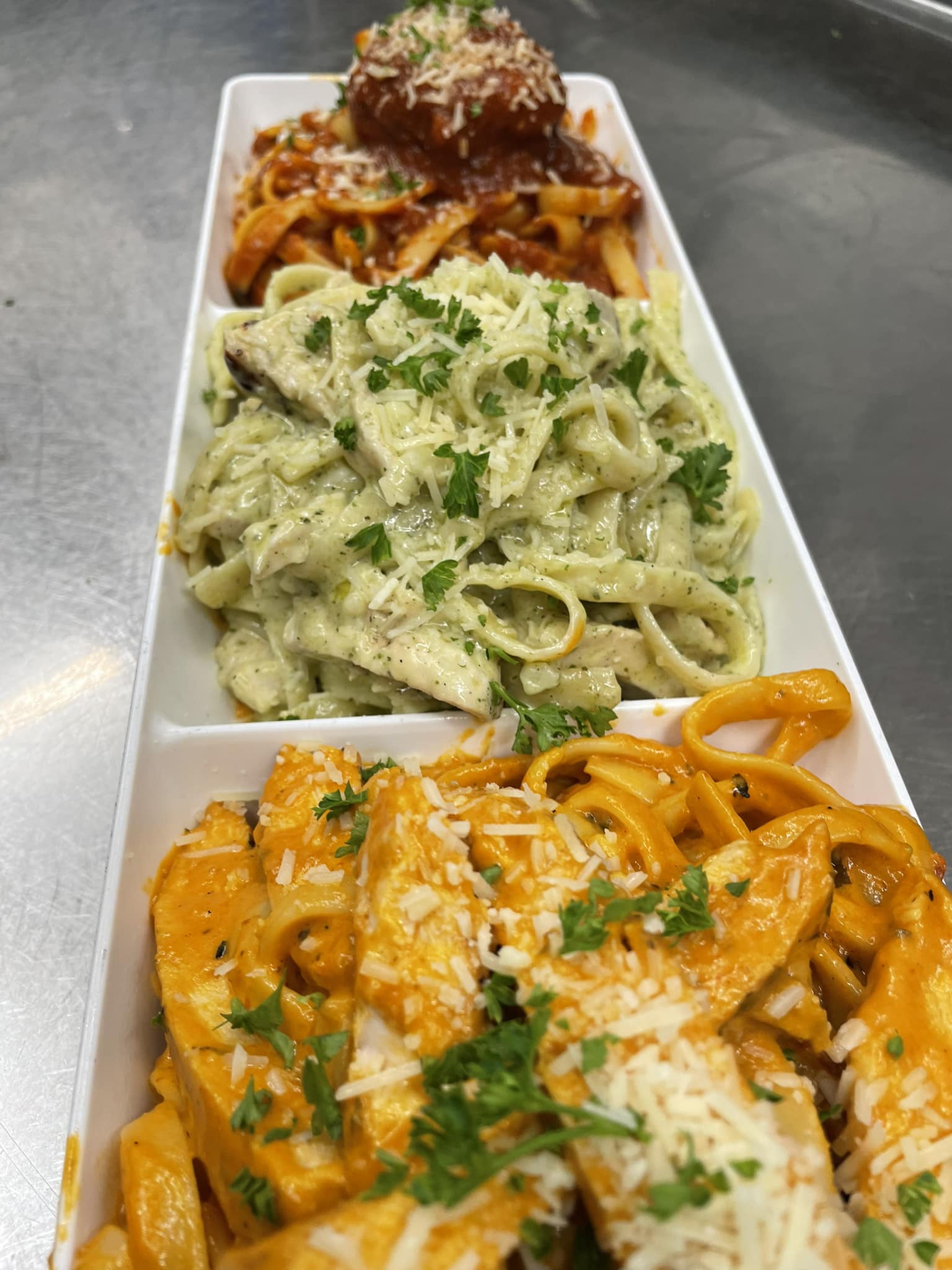 Three pasta dishes on white platter: pesto, tomato, and creamy sauces