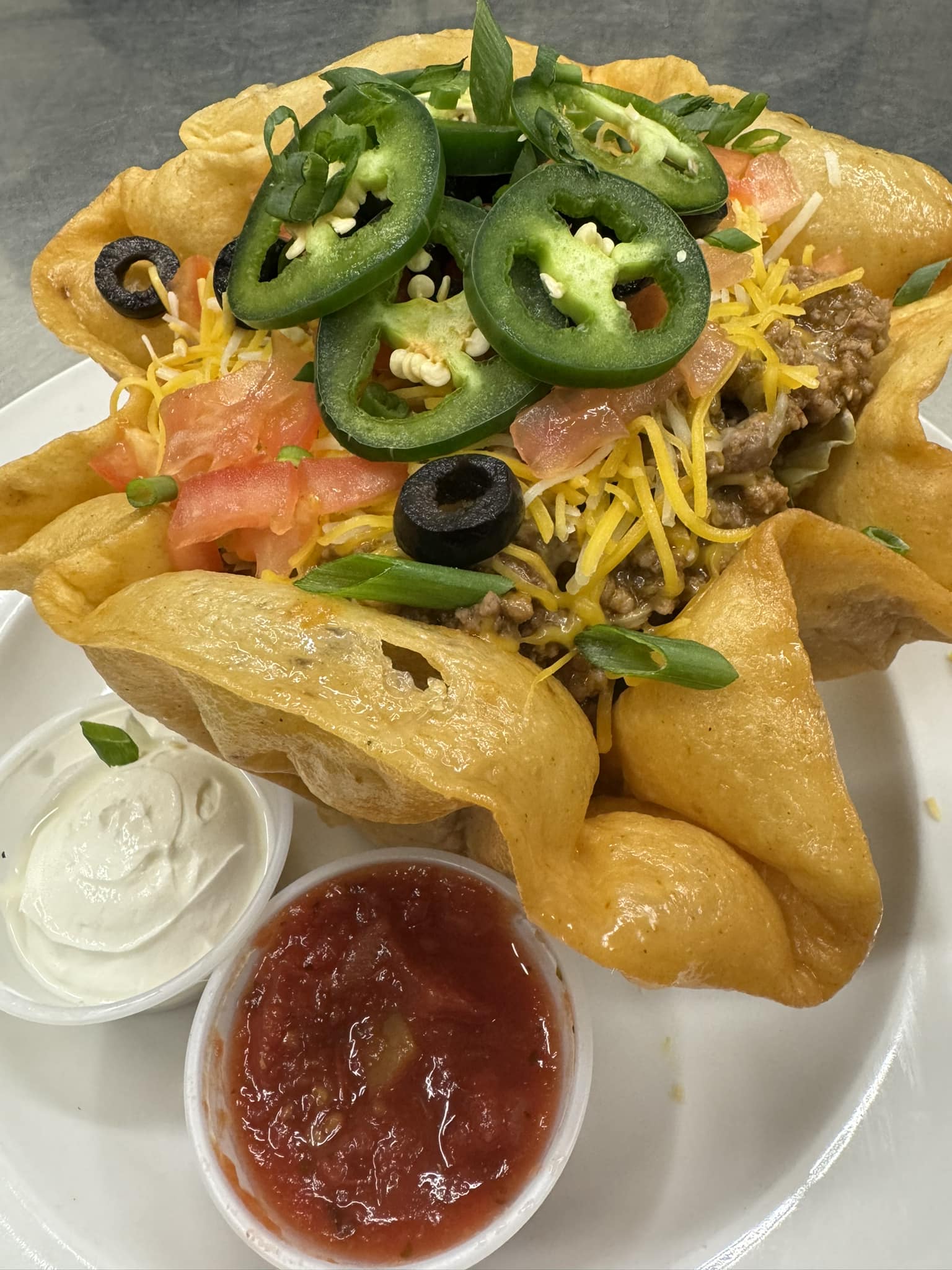 Crispy taco shell bowl filled with seasoned beef, cheese, jalapeños, tomatoes, and olives with salsa and sour cream