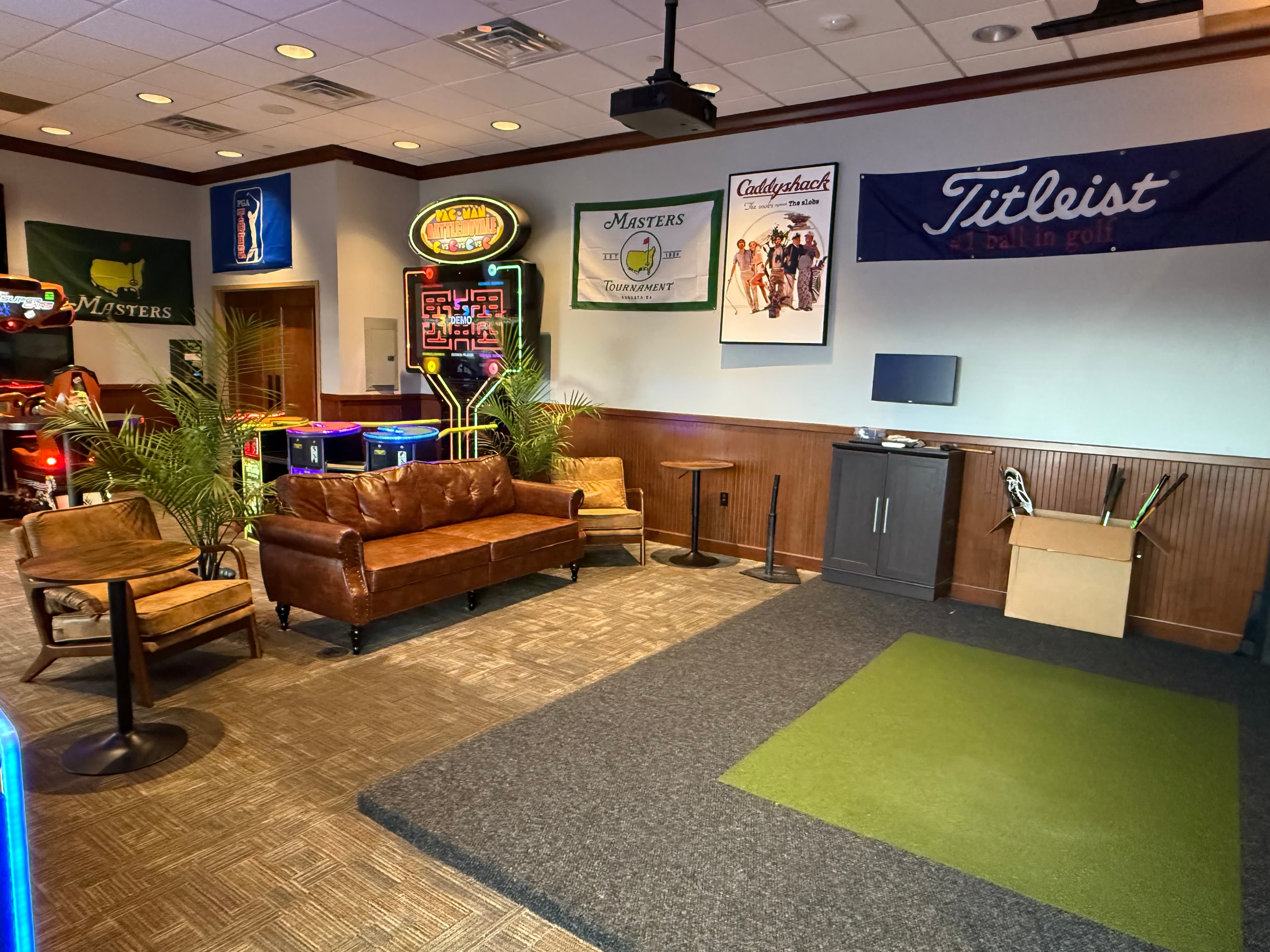 Lounge area with leather sofas, arcade games, and golf memorabilia including Masters and Titleist branding