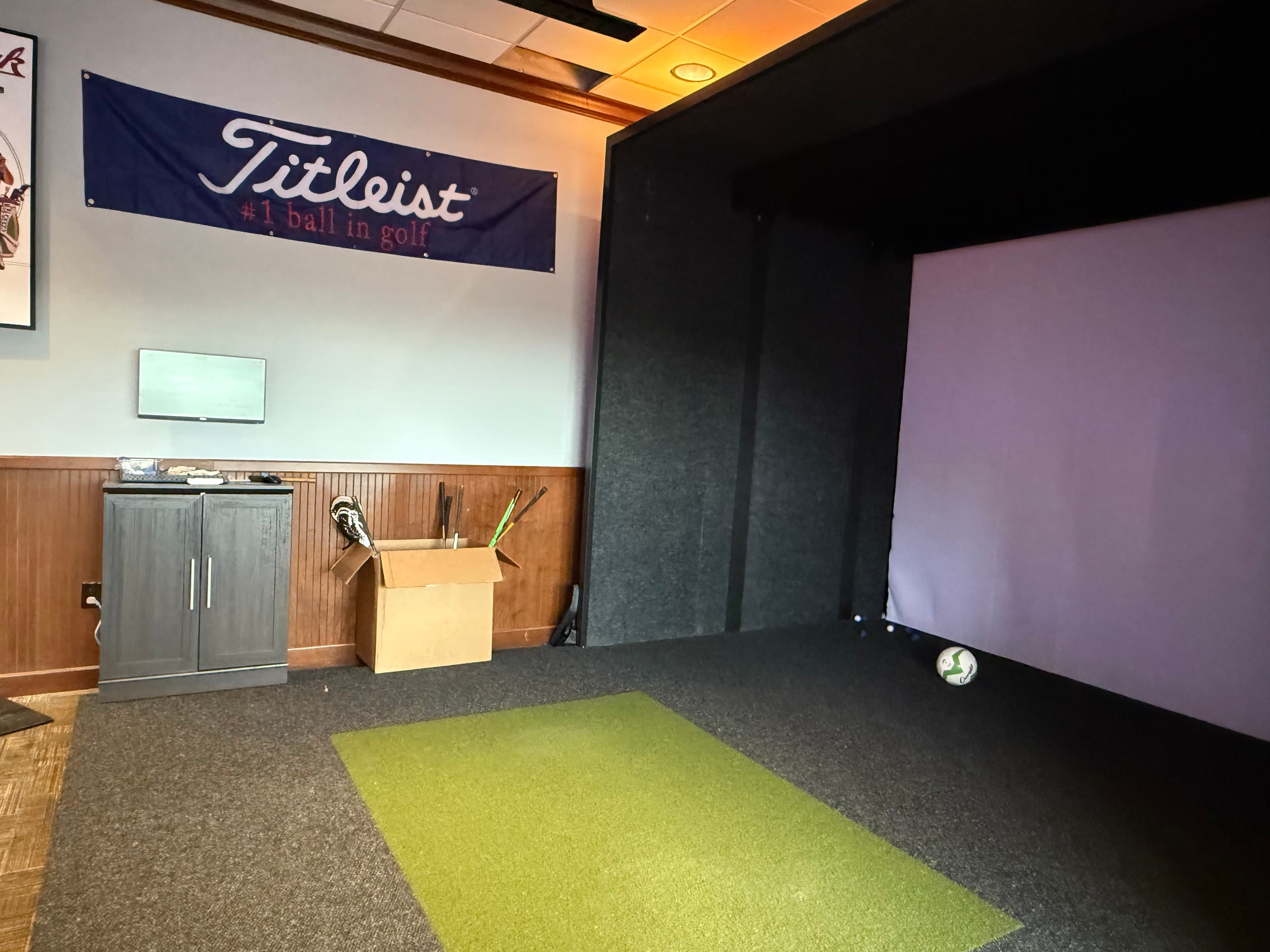 Titleist banner above indoor golf simulator with purple screen and green mat
